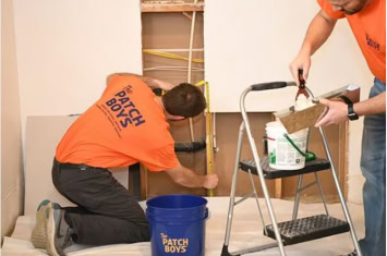 Two men from The Patch Boys repairing drywall inside a home